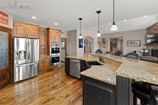 kitchen with a kitchen bar, pendant lighting, stainless steel appliances, and a stone fireplace