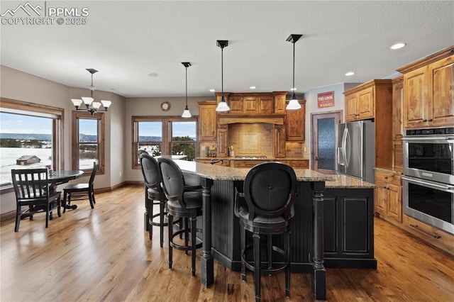 kitchen with a large island, light stone countertops, stainless steel appliances, and an inviting chandelier