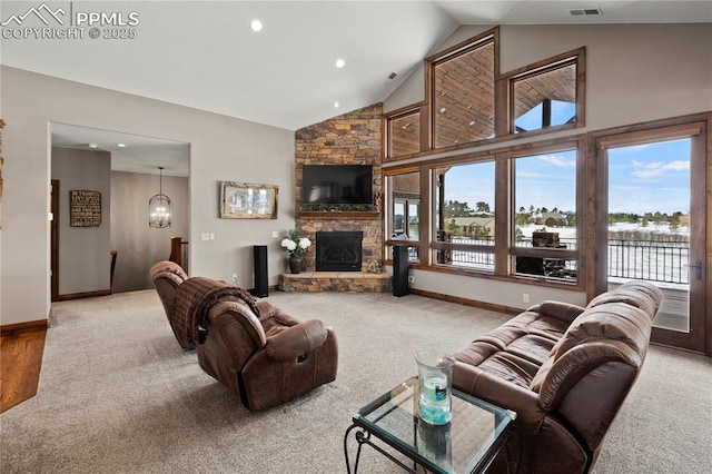 carpeted living room with a notable chandelier, a healthy amount of sunlight, a stone fireplace, and high vaulted ceiling