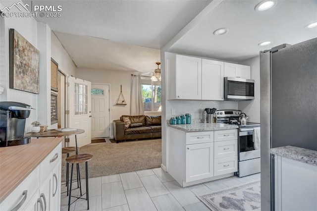 kitchen with light stone counters, stainless steel appliances, light carpet, and white cabinets