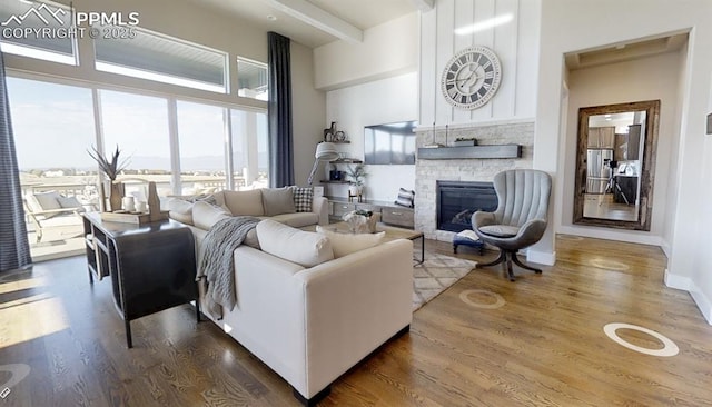 living room featuring beamed ceiling, baseboards, wood finished floors, and a fireplace