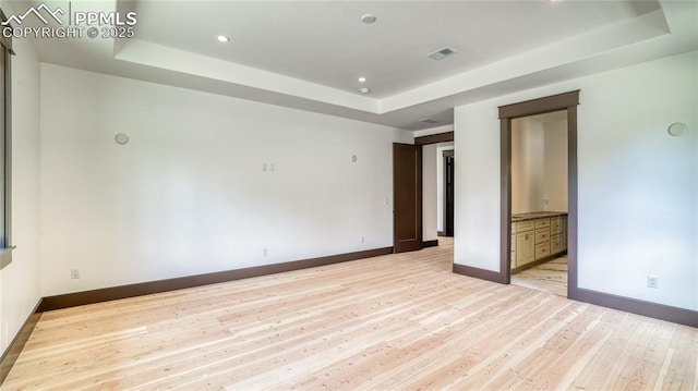 unfurnished bedroom featuring a raised ceiling, connected bathroom, and light hardwood / wood-style floors