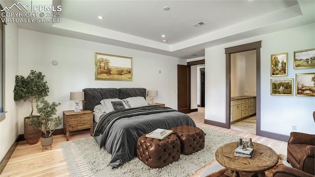 bedroom featuring a tray ceiling, ensuite bath, and light hardwood / wood-style flooring