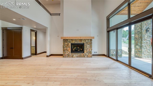 unfurnished living room with a high ceiling, light hardwood / wood-style floors, and a stone fireplace