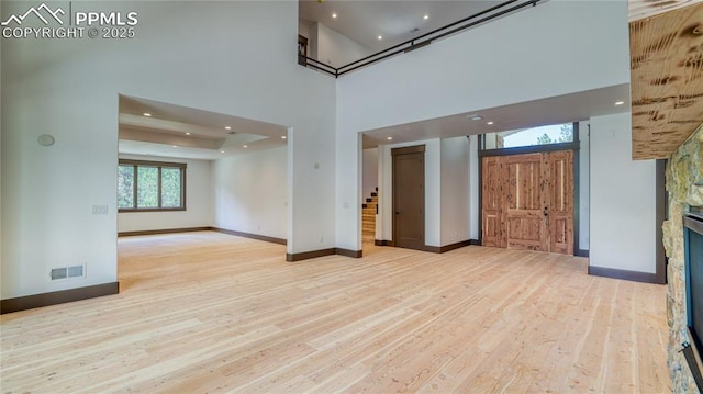 spare room with light wood-type flooring, a fireplace, and a high ceiling