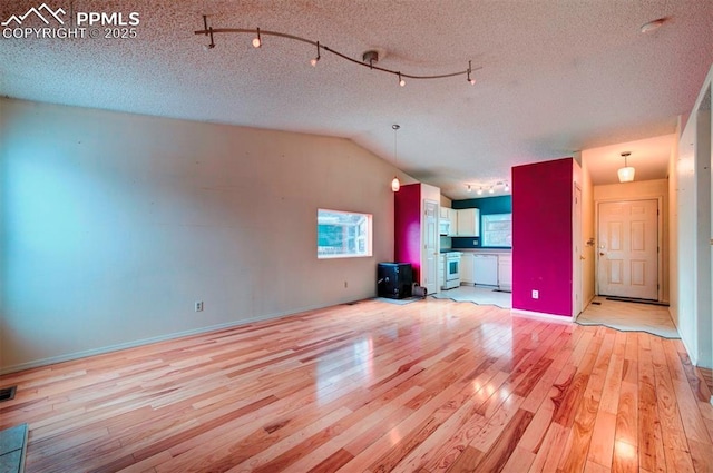 unfurnished living room with a textured ceiling, vaulted ceiling, and light wood-type flooring