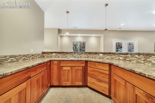 kitchen with pendant lighting, tasteful backsplash, light stone counters, and sink