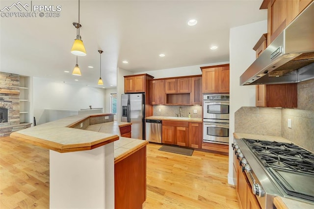 kitchen featuring exhaust hood, sink, decorative light fixtures, light hardwood / wood-style floors, and stainless steel appliances