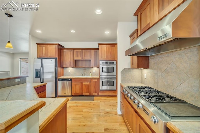 kitchen featuring stainless steel appliances, tile countertops, exhaust hood, and decorative light fixtures