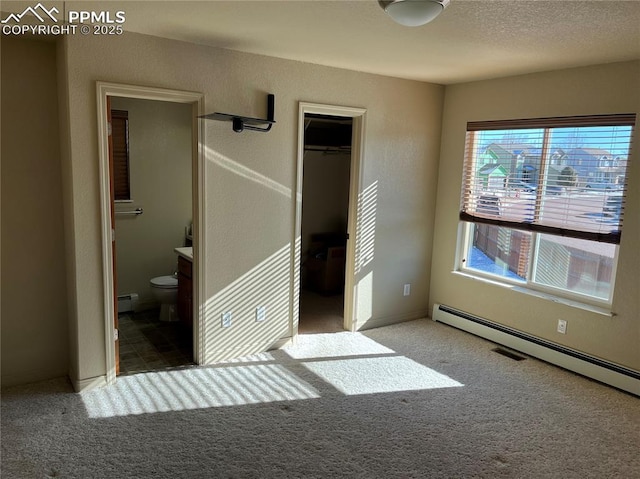 unfurnished bedroom with a closet, ensuite bath, carpet, a walk in closet, and a baseboard radiator