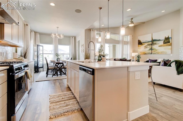 kitchen featuring stainless steel dishwasher, a kitchen island with sink, gas stove, and decorative light fixtures