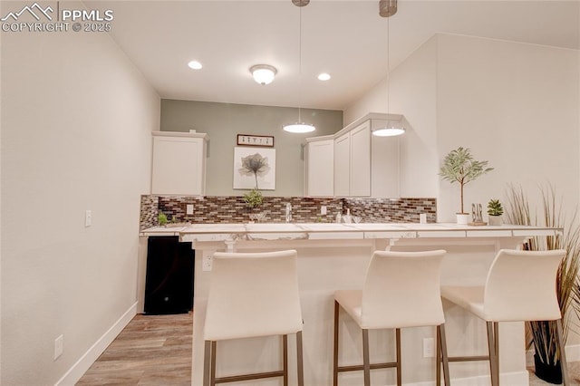 kitchen with a kitchen bar, decorative light fixtures, decorative backsplash, and white cabinets