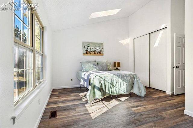 bedroom featuring high vaulted ceiling, a skylight, dark hardwood / wood-style floors, and a closet