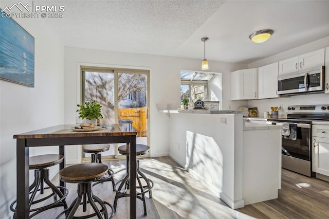 kitchen with white cabinetry, hardwood / wood-style floors, appliances with stainless steel finishes, a textured ceiling, and pendant lighting