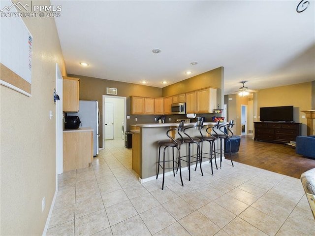 kitchen with a breakfast bar area, light tile patterned floors, light brown cabinets, appliances with stainless steel finishes, and kitchen peninsula