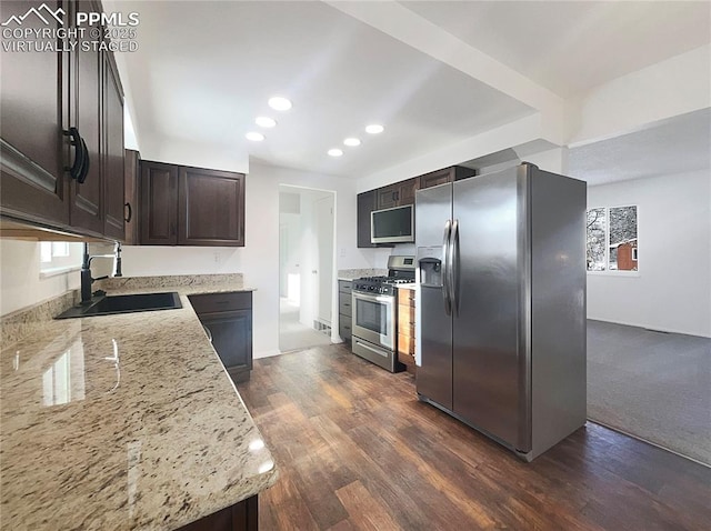 kitchen with light stone counters, dark brown cabinetry, stainless steel appliances, dark wood-type flooring, and sink