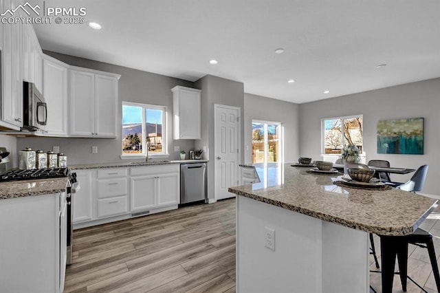 kitchen with a wealth of natural light, a center island, white cabinets, and appliances with stainless steel finishes