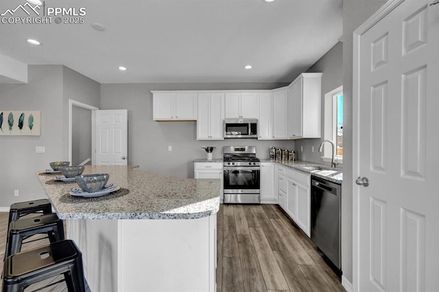 kitchen with sink, a kitchen island, light stone counters, white cabinetry, and stainless steel appliances