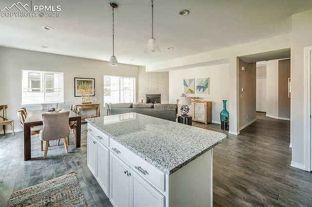 kitchen with light stone countertops, dark hardwood / wood-style flooring, pendant lighting, a center island, and white cabinetry