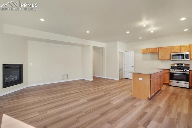 kitchen with light stone counters, a kitchen island, light wood-type flooring, and appliances with stainless steel finishes