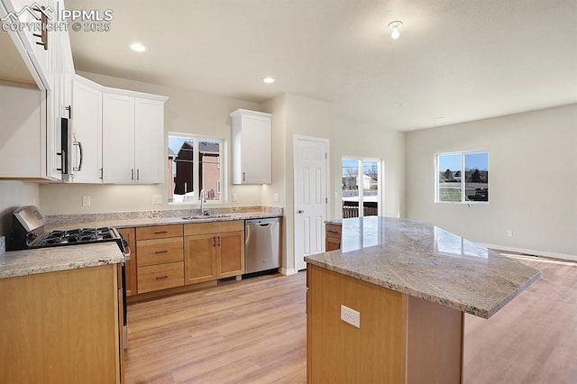 kitchen featuring light wood-type flooring, stainless steel dishwasher, sink, white cabinets, and a center island