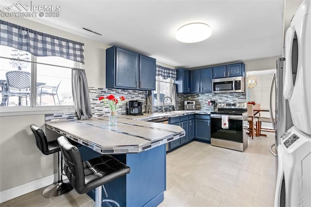 kitchen featuring blue cabinets, kitchen peninsula, appliances with stainless steel finishes, and a kitchen bar