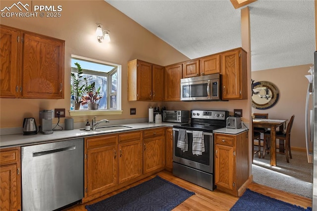 kitchen with vaulted ceiling, stainless steel appliances, light hardwood / wood-style flooring, and sink