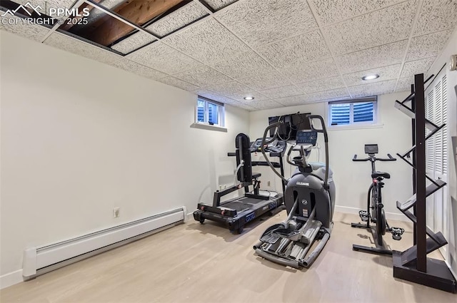 exercise area featuring wood-type flooring, a drop ceiling, and a baseboard radiator