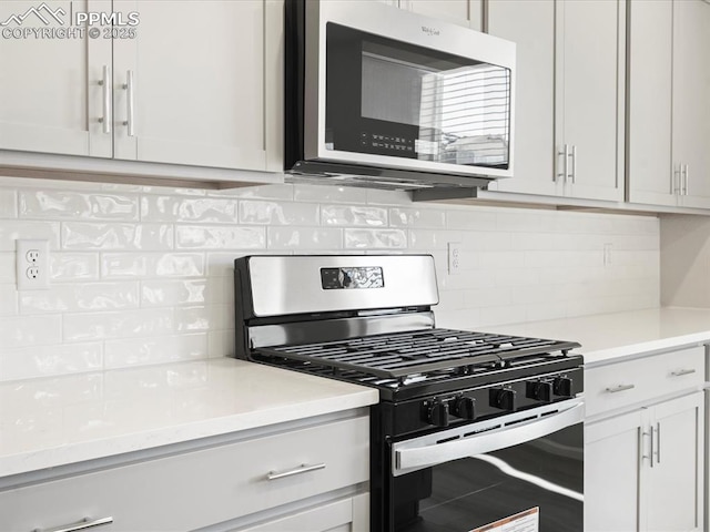 kitchen featuring gas range, backsplash, and white cabinets