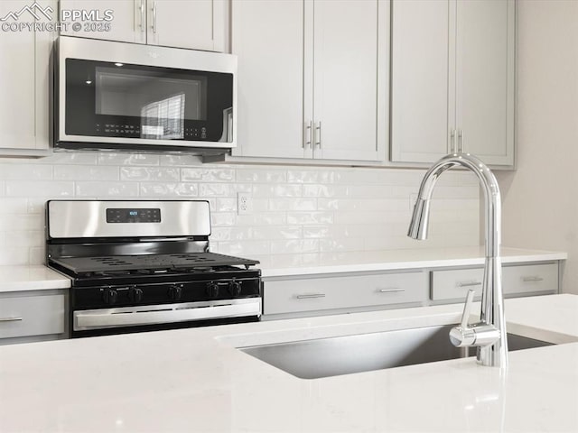 kitchen with sink, decorative backsplash, gray cabinets, and appliances with stainless steel finishes