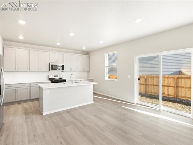 kitchen with sink, stainless steel electric range oven, light wood-type flooring, an island with sink, and decorative backsplash