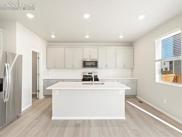 kitchen featuring sink, tasteful backsplash, light hardwood / wood-style flooring, appliances with stainless steel finishes, and a kitchen island with sink