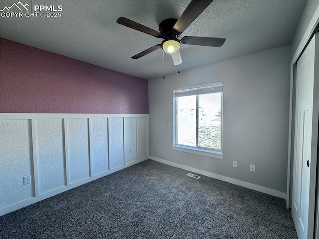 unfurnished bedroom featuring a closet, ceiling fan, a textured ceiling, and dark colored carpet