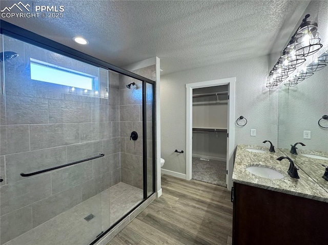 bathroom with toilet, a textured ceiling, hardwood / wood-style floors, an enclosed shower, and vanity