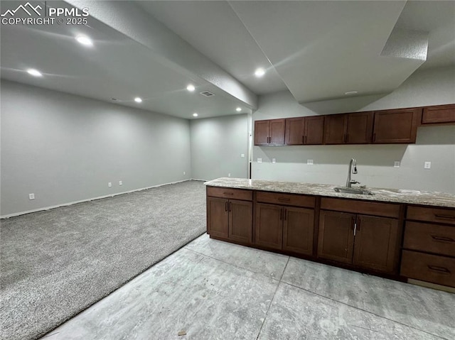 kitchen featuring sink, dark brown cabinetry, light stone counters, and light colored carpet