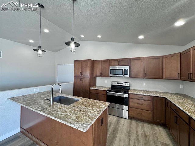 kitchen with appliances with stainless steel finishes, light wood-type flooring, pendant lighting, sink, and lofted ceiling