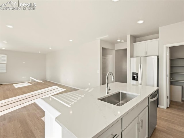 kitchen with a center island with sink, light wood-style flooring, stainless steel appliances, white cabinetry, and a sink