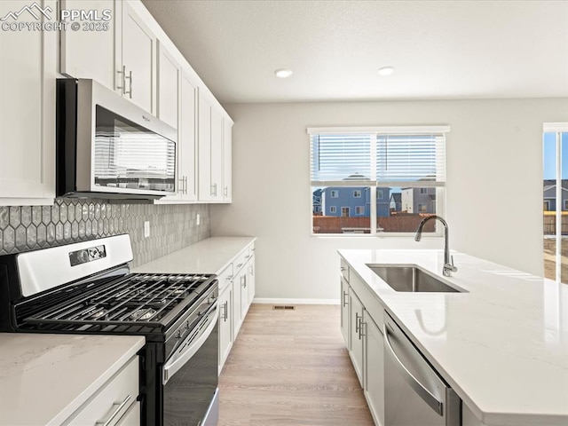 kitchen with light stone countertops, white cabinetry, stainless steel appliances, and a sink