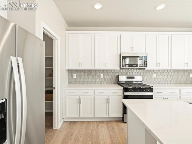 kitchen with stainless steel appliances, white cabinets, light wood finished floors, and tasteful backsplash