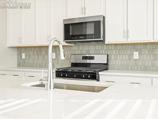 kitchen with light stone counters, stainless steel appliances, decorative backsplash, white cabinets, and a sink