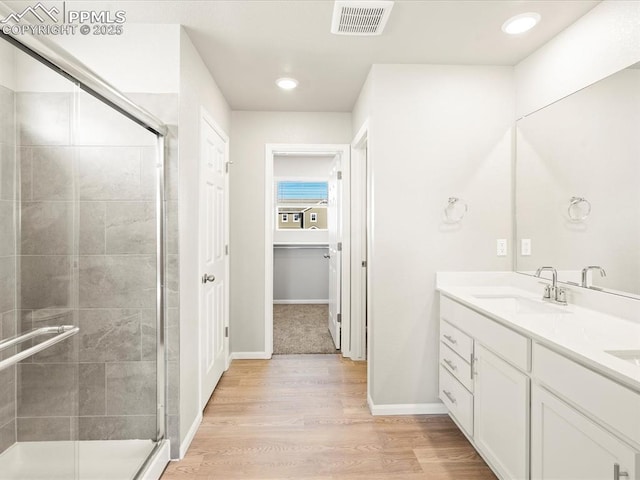 full bath featuring double vanity, visible vents, wood finished floors, a shower stall, and a sink