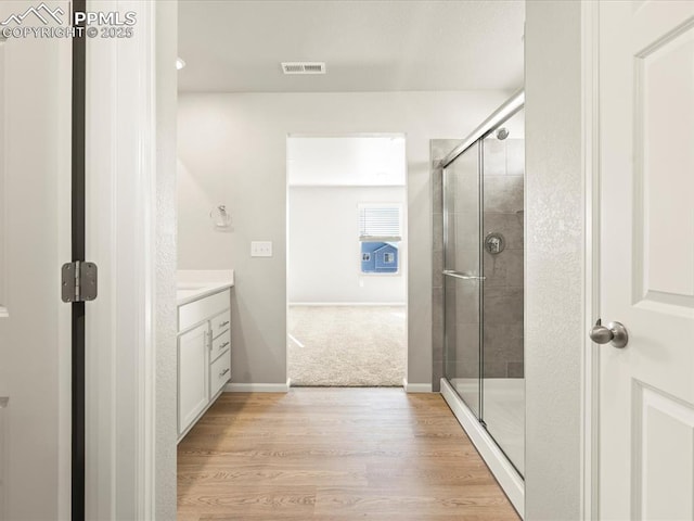 bathroom featuring wood finished floors, vanity, visible vents, baseboards, and a stall shower