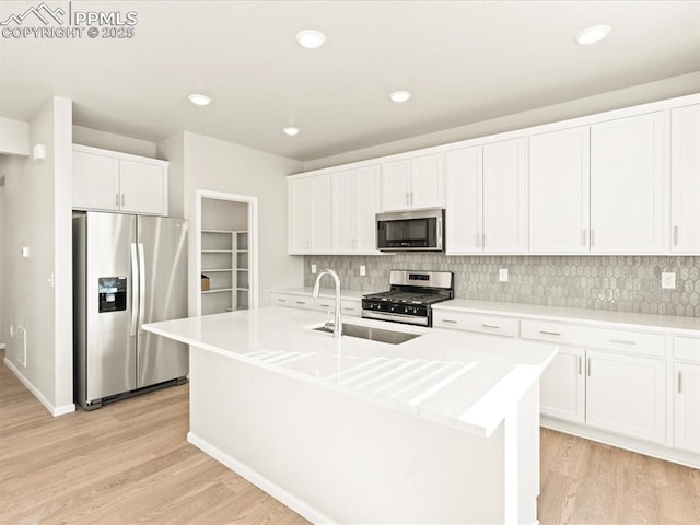 kitchen with stainless steel appliances, light countertops, a center island with sink, and white cabinets