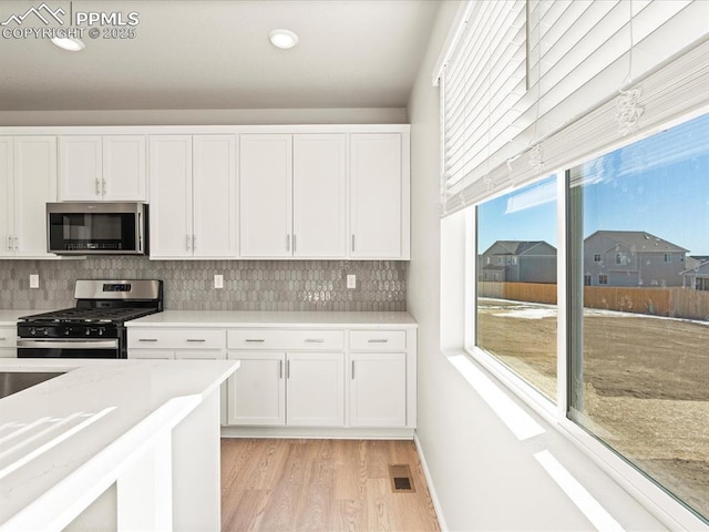 kitchen featuring visible vents, light wood-style floors, white cabinets, appliances with stainless steel finishes, and tasteful backsplash