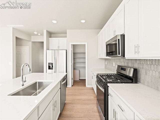 kitchen with appliances with stainless steel finishes, white cabinetry, a sink, and light stone countertops