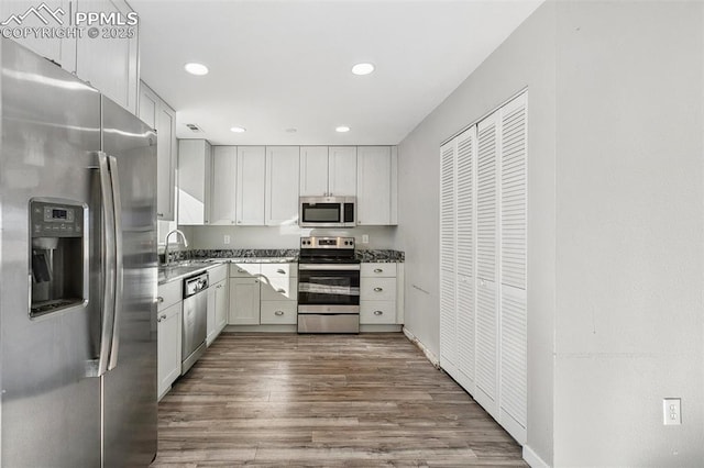 kitchen featuring white cabinetry, sink, dark wood-type flooring, dark stone countertops, and appliances with stainless steel finishes