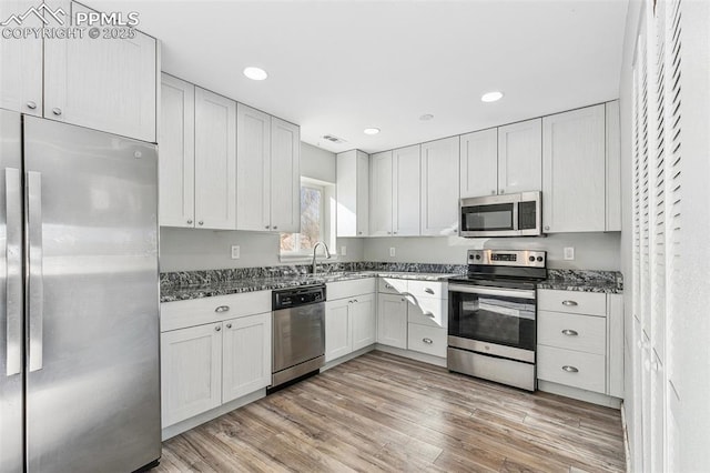 kitchen with dark stone countertops, light hardwood / wood-style flooring, white cabinets, and stainless steel appliances