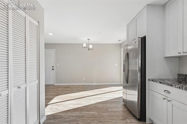 kitchen with dark wood-type flooring, white cabinets, stainless steel fridge, dark stone countertops, and decorative light fixtures