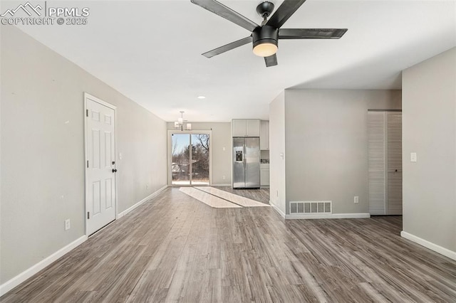 unfurnished living room featuring wood-type flooring and ceiling fan with notable chandelier