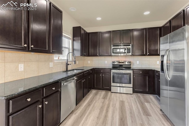 kitchen featuring dark stone countertops, stainless steel appliances, dark brown cabinets, sink, and light hardwood / wood-style flooring